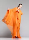 Beautiful woman in long orange dress posing dramatic in the studio