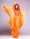 Beautiful woman in long orange dress posing dramatic in the studio