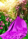 Beautiful Woman in long Purple Dress in Flower Garden Rear View. Fantasy Girl walking away in Spring Blossom Park enjoying Sun Royalty Free Stock Photo