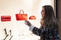 Beautiful woman looks at a shop window with accessories. Young blonde in a stylish coat and with a red bag. Style and fashion Royalty Free Stock Photo