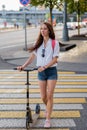 Beautiful woman with lush and long hair, in summer in city crosses road crossing on zebra. Scooter shorts and shirt with Royalty Free Stock Photo