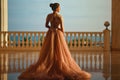 Beautiful woman in luxurious ballroom dress with tulle skirt and lacy top standing on the large balcony with sea view