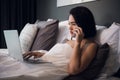 Beautiful woman lying in bed and making a phone call. Young girl using her laptop at home. Beautiful woman relaxing at Royalty Free Stock Photo