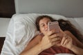 Girl with long hair lies bed looks into phone Royalty Free Stock Photo