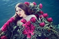 Beautiful woman lying in the wooden boat covered with huge pile of peonies