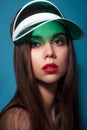 Beautiful woman with make-up and red lips in green gel cap visor on the blue background Royalty Free Stock Photo