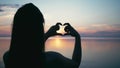 Beautiful Woman making heart shape with hands at sunset Girl holding up love symbol gesture with orange sun flare