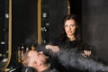 Beautiful woman male master hairdresser steams man's beard with steam and towel in barber shop