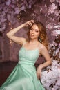 Beautiful woman model in a mint-colored dress on a flowered spring background. Beauty girl with a stunning makeup and hairstyle Royalty Free Stock Photo