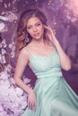 Beautiful woman model in a mint-colored dress on a flowered spring background. Beauty girl with a stunning makeup and hairstyle Royalty Free Stock Photo