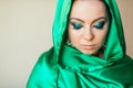 A beautiful woman of Oriental appearance with make up on her face in a shiny green scarf covering her head closed her eyes. Royalty Free Stock Photo