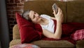 Beautiful woman in pajamas lying on sofa at living room and using smartphone. People relaxing at home, communications, remote work Royalty Free Stock Photo