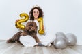 Beautiful woman in pajamas and smiling at the camera celebrating New Year`s Eve with her dog and some balloons at home. The dog i