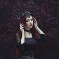 A beautiful woman with pale skin and long red hair in a black dress and in the black crownk. Girl witch with vampire Royalty Free Stock Photo