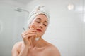 Beautiful woman with perfect skin wearing white towel after shower, making face massage using a jade face roller with natural Royalty Free Stock Photo