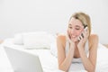 Beautiful woman phoning while lying on her bed using her notebook Royalty Free Stock Photo