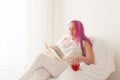 Beautiful woman with pink hair reading a book in a white room Royalty Free Stock Photo