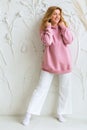 Beautiful woman in pink hoodie and white pants posing against white wall background Royalty Free Stock Photo