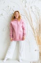 Beautiful woman in a pink hoodie and white pants posing against a background of a white wall. Royalty Free Stock Photo