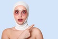 Beautiful woman before plastic surgery with bandaged face. Girl looks shocked, points fore finger aside, with opened mouth and Royalty Free Stock Photo