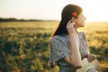 Beautiful woman with poppy flower behind ear relaxing in barley field in sunset light. Stylish female standing in evening summer Royalty Free Stock Photo