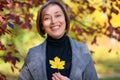 Beautiful woman portrait, she holds a yellow leaf and laughs merrily, posing in autumn city park, bright sunny day Royalty Free Stock Photo