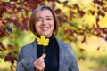 Beautiful woman portrait, she holds a yellow leaf and laughs merrily, posing in autumn city park, bright sunny day Royalty Free Stock Photo