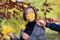 Beautiful woman portrait, she holds a yellow leaf and laughs, the other hand covers her face with a maple leaf, posing in autumn Royalty Free Stock Photo