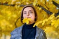 Beautiful woman portrait, she put the maple leaf in her mouth and is surprised, posing in autumn city park, bright sunny day Royalty Free Stock Photo