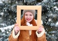 Beautiful woman portrait on winter outdoor, look through wooden frame, snowy fir trees in forest, long red hair, wearing a sheepsk Royalty Free Stock Photo