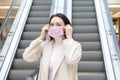 Beautiful woman putting on pink medical mask on her face against the background of the escadator in a public place Royalty Free Stock Photo