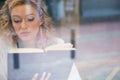 Beautiful woman reading book seen through cafe window Royalty Free Stock Photo