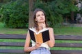 Beautiful woman is reading a book and thinking about something on the bench in the park. Girl has some thoughts and ideas Royalty Free Stock Photo