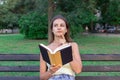 Beautiful woman is reading a book and thinking about something on the bench in the park. Girl has some thoughts and ideas Royalty Free Stock Photo