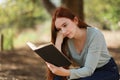 Beautiful woman reads a book sitting under the shade of a tree Royalty Free Stock Photo