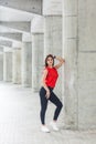 Beautiful woman in red blouse and jeans posing while leaning on gray column