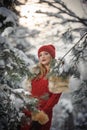 Beautiful woman in red with brown fur cape enjoying the winter scenery in forest. Blonde girl posing under snow-covered trees Royalty Free Stock Photo