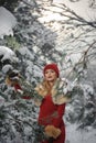 Beautiful woman in red with brown fur cape enjoying the winter scenery in forest. Blonde girl posing under snow-covered trees Royalty Free Stock Photo