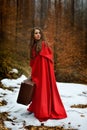 Beautiful woman with red cloak and suitcase alone in the woods