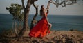 Beautiful woman in red dress on the sea shore cliff during over sea and sky background Royalty Free Stock Photo