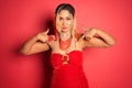 beautiful woman in red with gold necklace pointing upwards over red wall Royalty Free Stock Photo