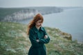 Beautiful woman with red hair on a cliff of a mountain near the sea, wind, sadness Royalty Free Stock Photo