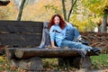 Beautiful woman with red hair sits on a bench and reads a book that lies nearby. Autumn park background. Nearby is a warm blanket Royalty Free Stock Photo