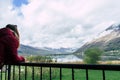 Beautiful woman in a red jacket dress at sunset on a background of mountains and a lake. Relax girl in a balcony with cloudy sky Royalty Free Stock Photo