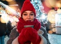 Beautiful Woman in Red Scarf and Hat Holding in Red Mittens Hot Mulled Wine and Smiling at European Christmas Market