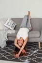 Beautiful woman relaxing on a grey couch with head upside down. Cute girl having fun at cozy home in lazy day. Royalty Free Stock Photo