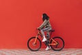 Beautiful woman rides a bicycle on a background of a red wall, looking ahead at the copy space. Hispanic woman standing on a