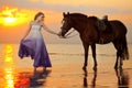 Beautiful woman riding a horse at sunset on the beach. Young girl with a horse in the rays of the sun by the sea. Royalty Free Stock Photo