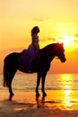 Beautiful woman riding a horse at sunset on the beach. Young girl with a horse in the rays of the sun by the sea. Royalty Free Stock Photo