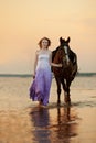 Beautiful woman riding a horse at sunset on the beach. Young girl with a horse in the rays of the sun by the sea. Royalty Free Stock Photo